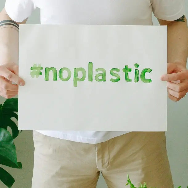 Person holding a sign with '#no plastic' text, surrounded by greenery