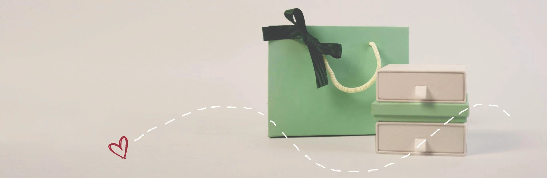 Green gift bag with a black ribbon and beige jewelry box on a light background