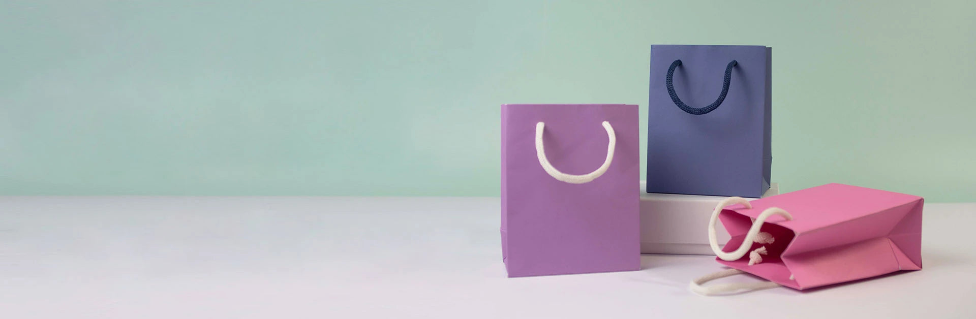 Three colorful paper shopping bags on a light green background