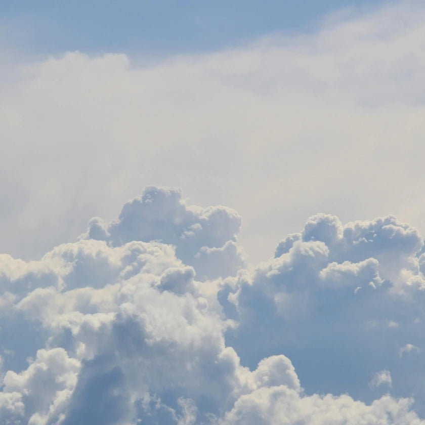 Fluffy white clouds float against a bright blue sky, creating a serene and peaceful atmosphere. The soft, billowing shapes suggest calm weather.