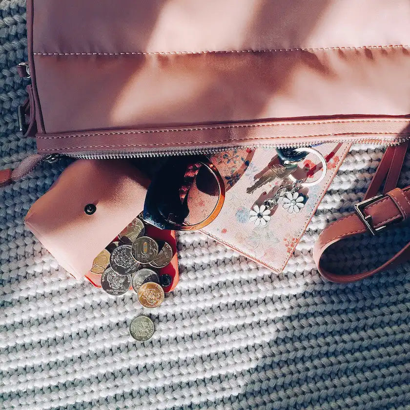 Pink handbag with coins and sunglasses on a textured surface
