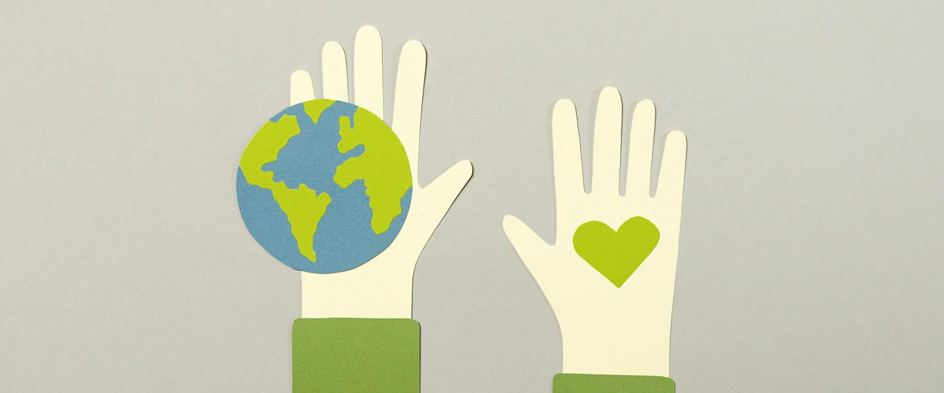 Two paper cutout hands on a grey background; one holds a globe, the other has a green heart. The image conveys themes of care and environmentalism.
