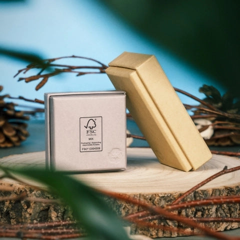 A silver jewellry box and a beige jewellry box rest on a wooden surface surrounded by pinecones and branches, conveying an eco-friendly, natural vibe.