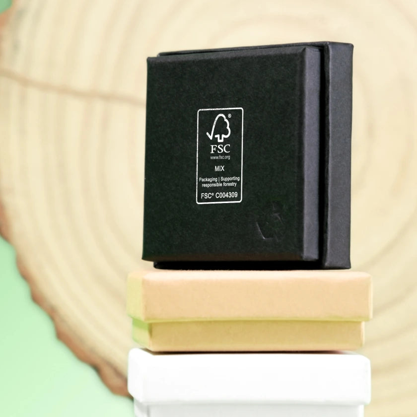 A black FSC-certified box sits on tan and white boxes, in front of a wood-like background. The image conveys sustainability and eco-friendliness.