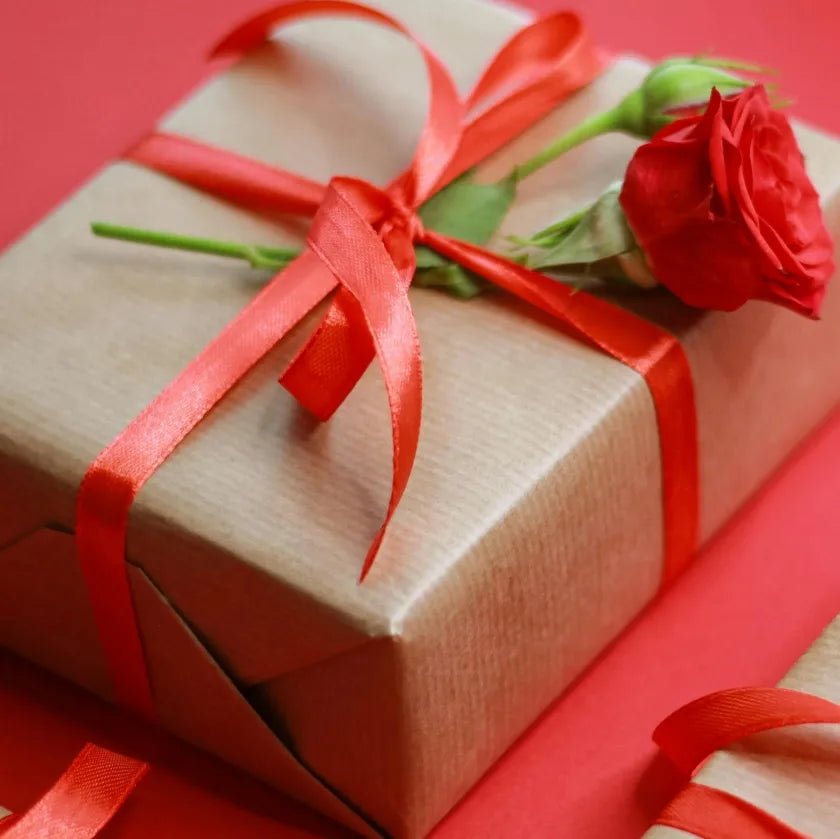 A brown gift with red ribbon and a rose placed gently on top. Red background.
