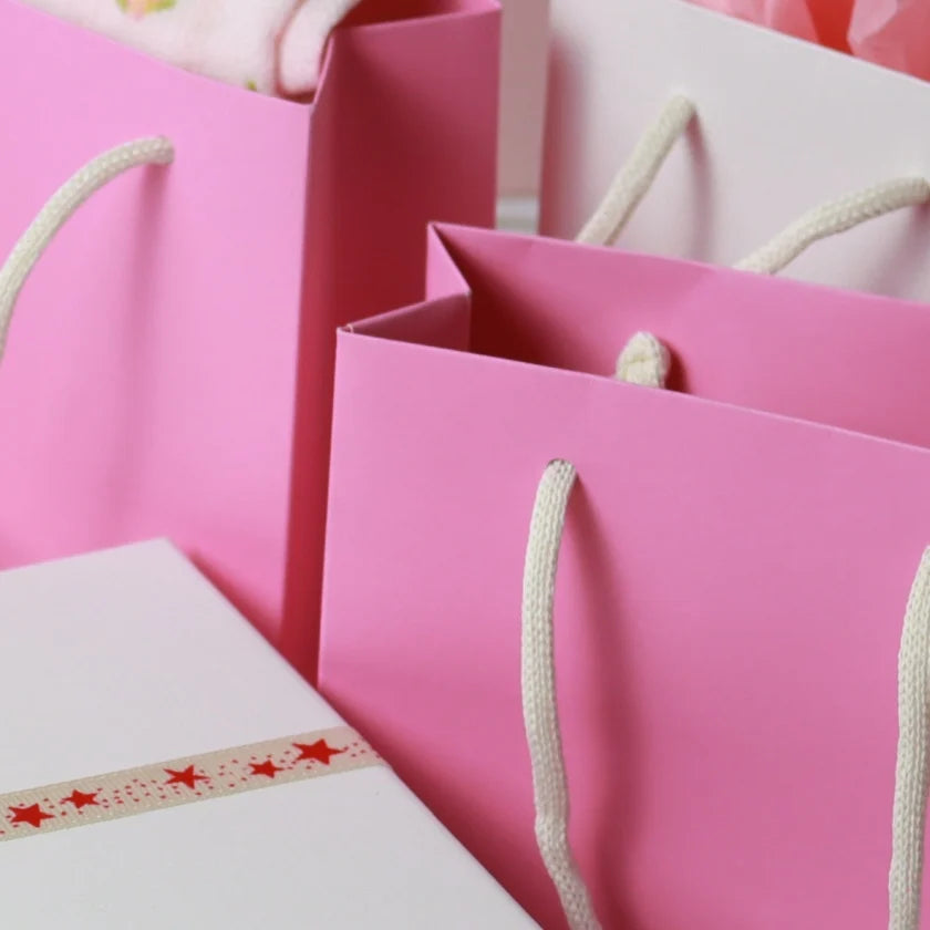 Pink gift bags with white rope handles sit beside a gift box wrapped in white star-patterned ribbon.