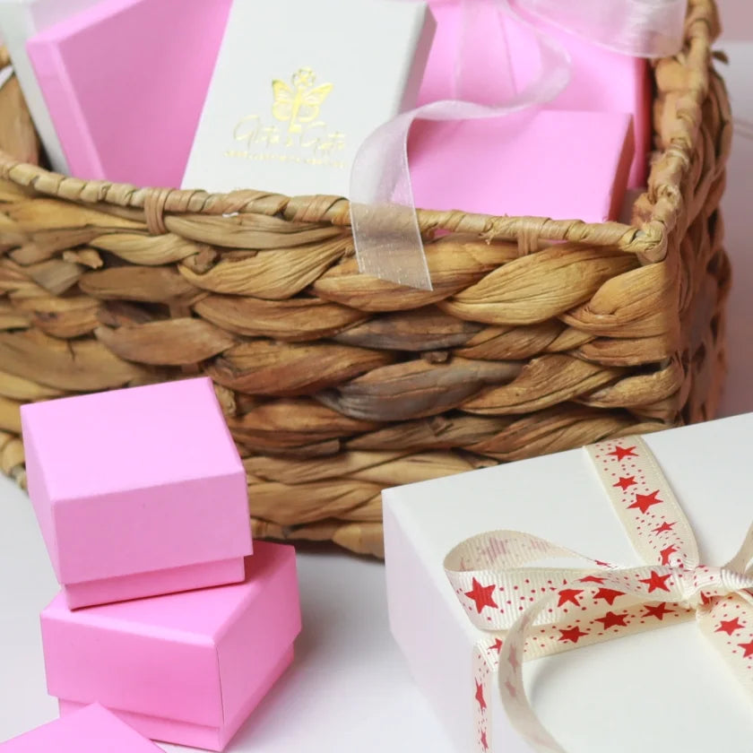 A woven basket filled with pink gift boxes. Accompanied by a larger white gift box, wrapped with star-patterned ribbon.