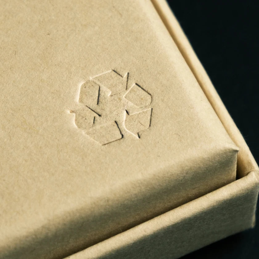 A close-up of a kraft jewellry box with an embossed recycling symbol. 