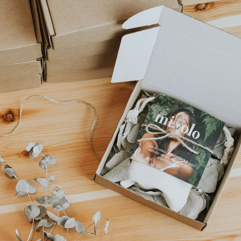 Open box with a magazine titled 'miolo' on a wooden surface with eucalyptus leaves.