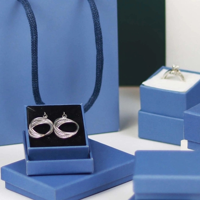 Elegant silver earrings in a blue gift box, accompanied by a ring on a stand, surrounded by additional blue boxes, evoking a sense of luxury.