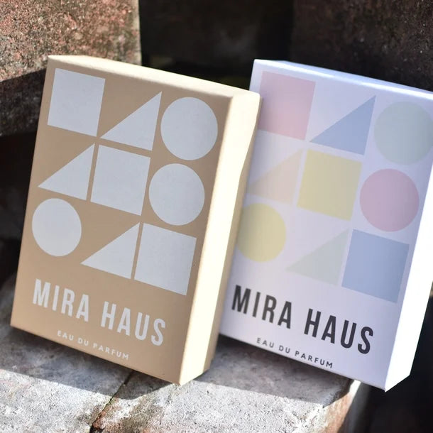 Two MIRA HAUS eau du parfum gift boxes with geometric designs on a stone surface.