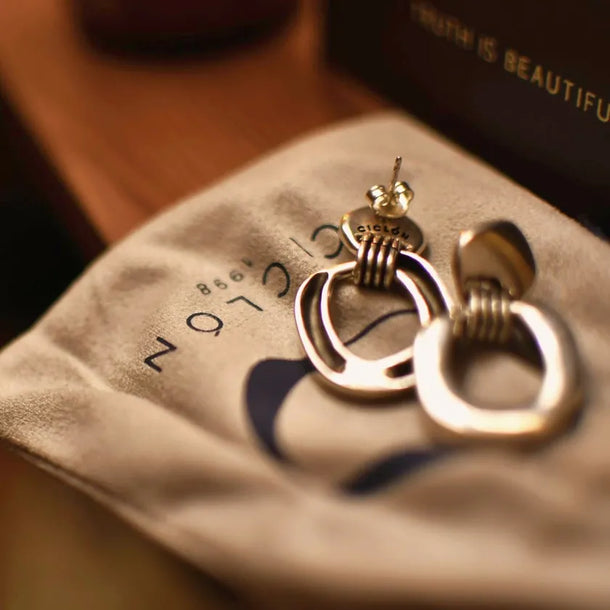 Pair of gold hoop earrings on a soft fabric surface with 'SOPHIE' branding.