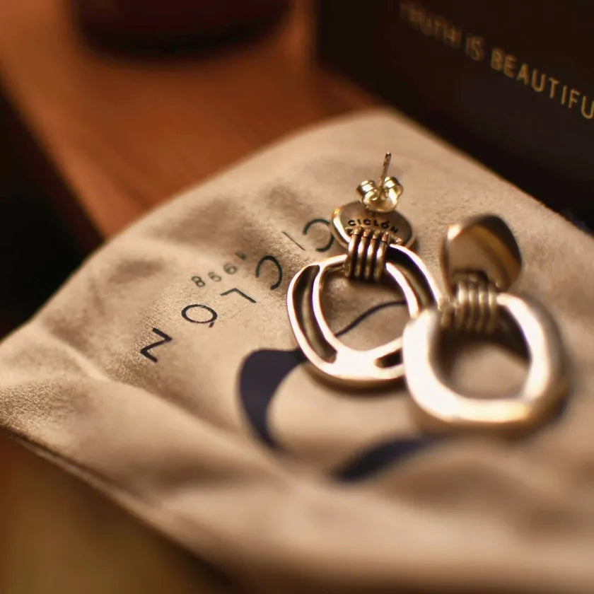 Pair of gold hoop earrings on a soft fabric surface with 'SOPHIE' branding.