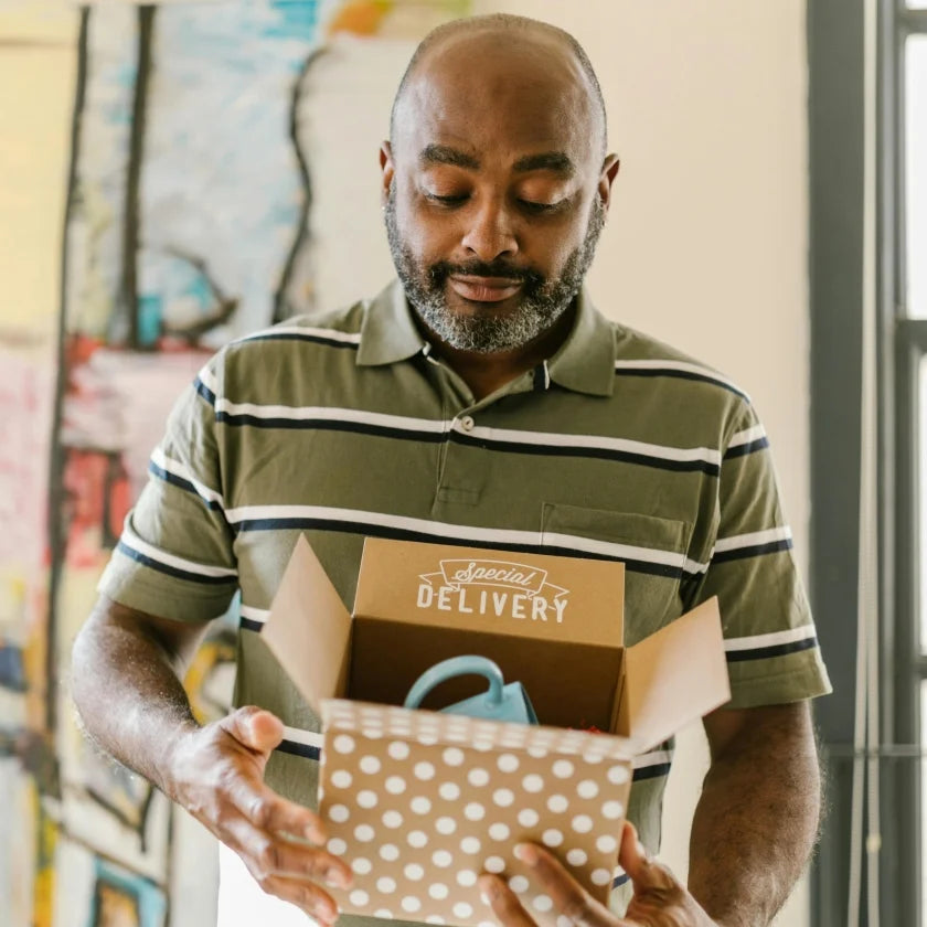 Man in striped shirt looks at an open gift box labeled 