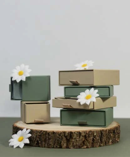 Stacked green and beige drawer boxes on a wooden slice, each adorned with white daisies