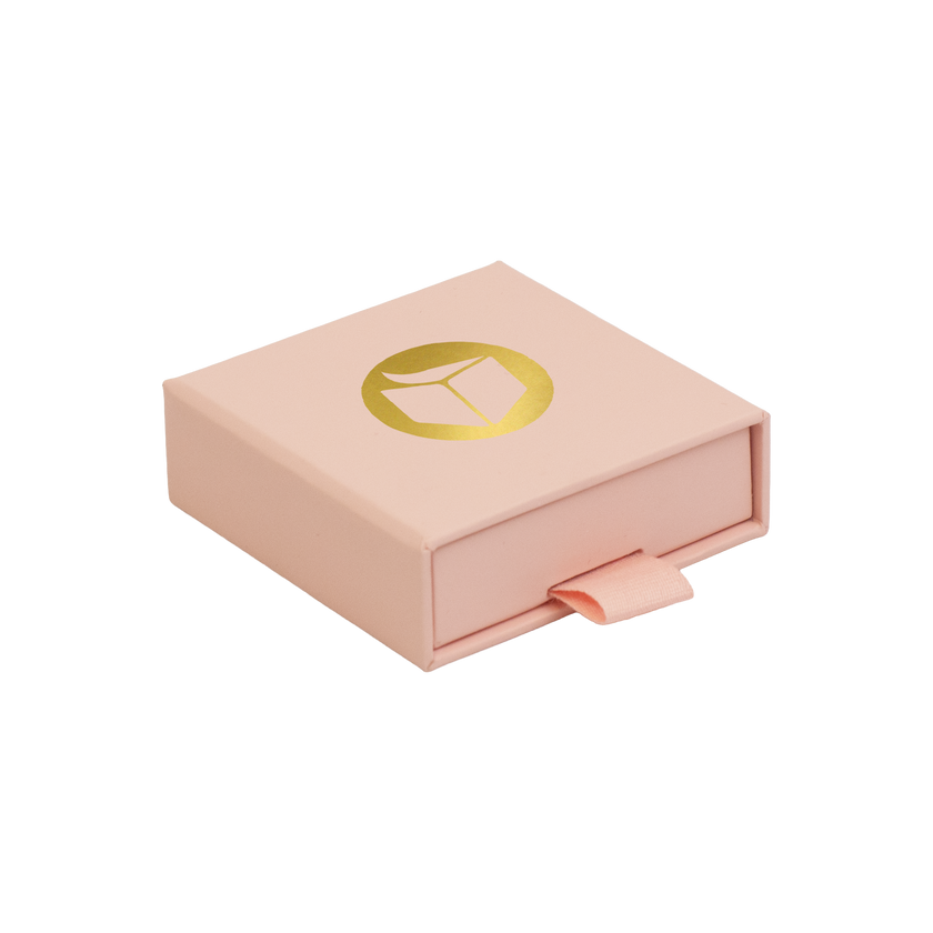 A light pink square gift box with a pull tab and a gold circular logo on top, shown on a plain white background.