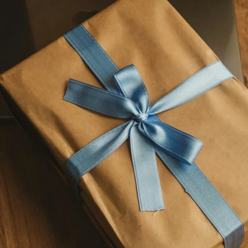 A gift wrapped in brown paper with a shiny blue ribbon tied in a bow on a wooden surface, evoking a simple, elegant, and festive mood.