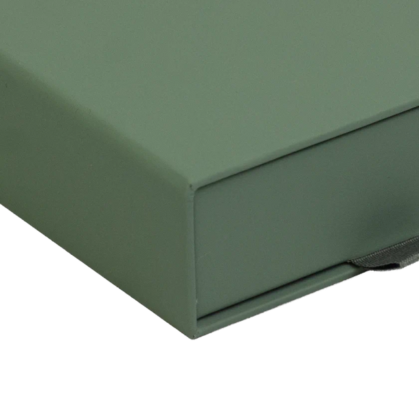 A close-up of a matte sage green box corner with a dark elastic band visible on the right side, isolated on a white background.