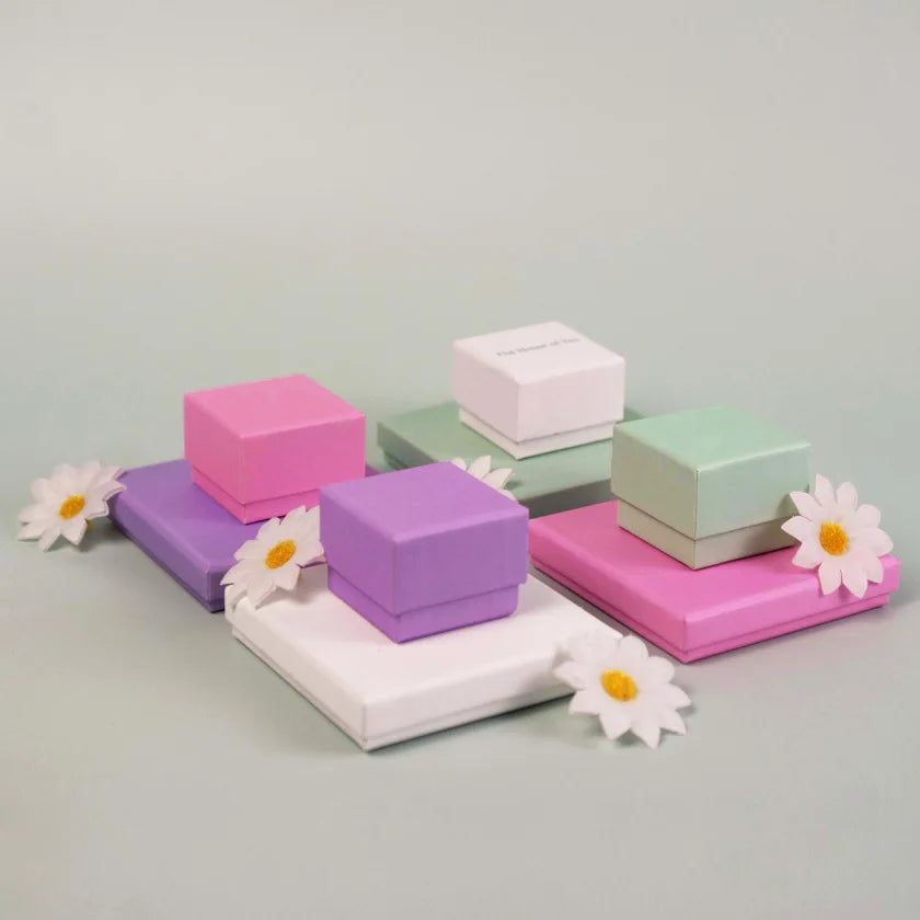 Small square jewellery boxes in shades of pink, purple, white, and green, decorated with artificial daisy flowers.