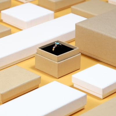 A diamond ring in an open kraft gift box is surrounded by various closed gift boxes on a yellow background, conveying elegance.