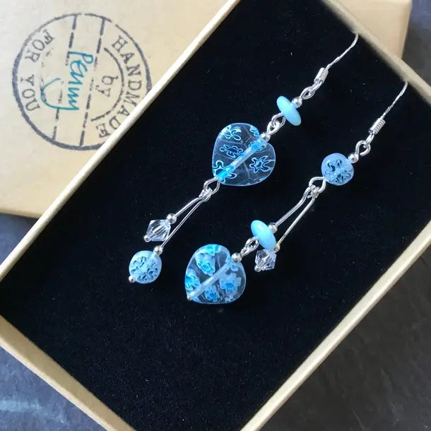 Blue beaded earrings in a jewellery box with 'Penny Handmade' branding.