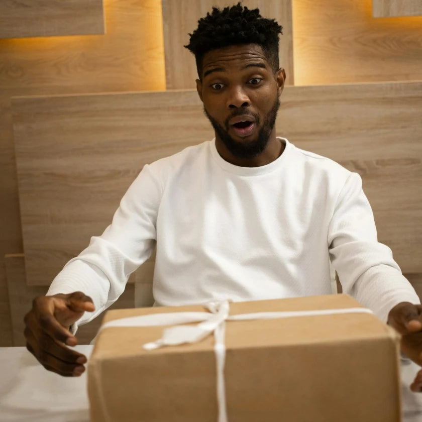 Man in white shirt looks surprised at a gift-wrapped box on the table. Wooden background with warm lighting creates an atmosphere of excitement.